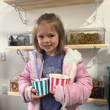 Young girl holding two striped cups, smiling indoors.