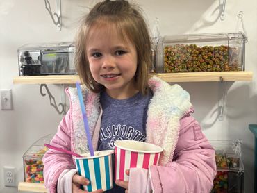 Young girl holding two striped cups, smiling indoors.