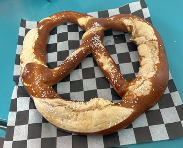 Large soft pretzel sprinkled with salt on checkered paper.