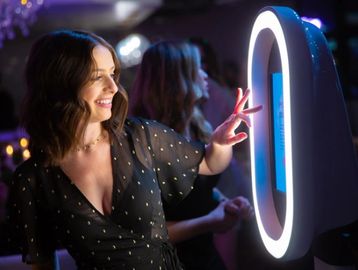 Woman smiling and interacting with a touchscreen photo booth at a party.