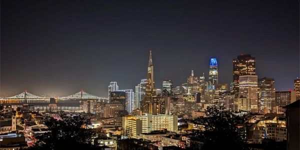 San Francisco skyline illuminated at night with Bay Bridge in view.
