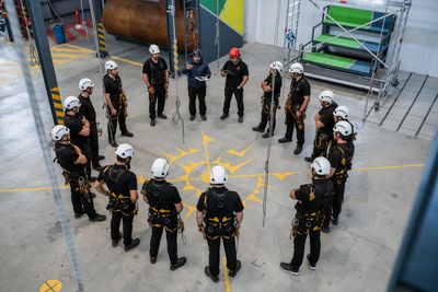 Group of people in helmets and harnesses standing in a circle indoors.