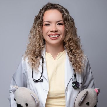 Smiling female doctor with curly hair and stethoscope holding stuffed animals.
