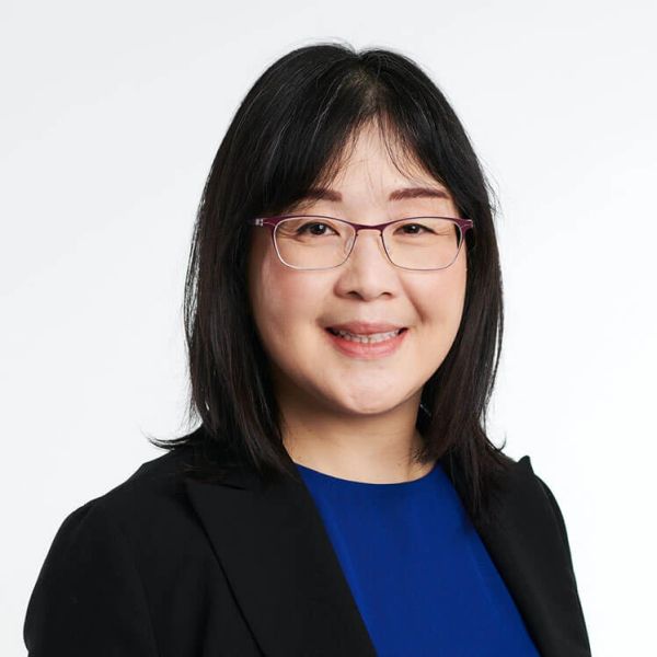 Professional portrait of a smiling woman with glasses, black hair, and business attire.