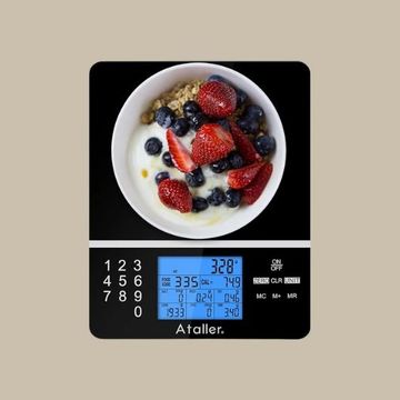 bowl of yogurt sits on a digital food scale. The scale’s blue display shows nutritional data
