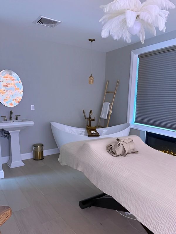 Spa room with a treatment bed, bathtub, and sink.