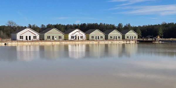 Row of houses reflected on calm water under a clear blue sky.