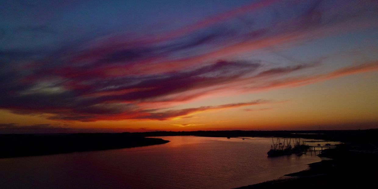 A vibrant sunset over a calm river with boats docked at the shore.