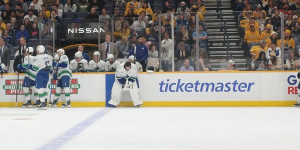 Hockey players on the bench during a game with spectators in the background.