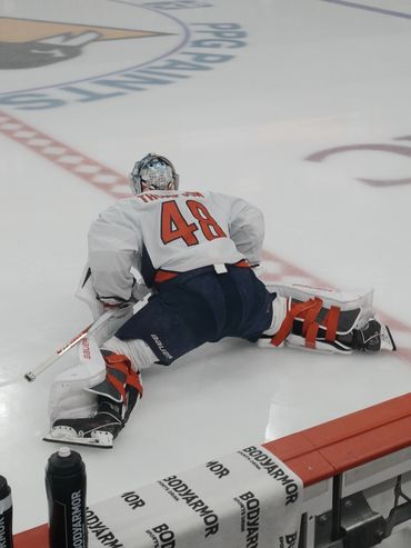 Hockey goalie in white jersey stretching before a game on ice rink.