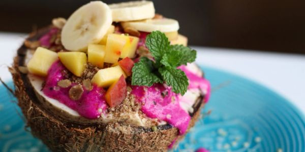 Tropical smoothie bowl with dragon fruit, banana, mango, and mint in a coconut shell.