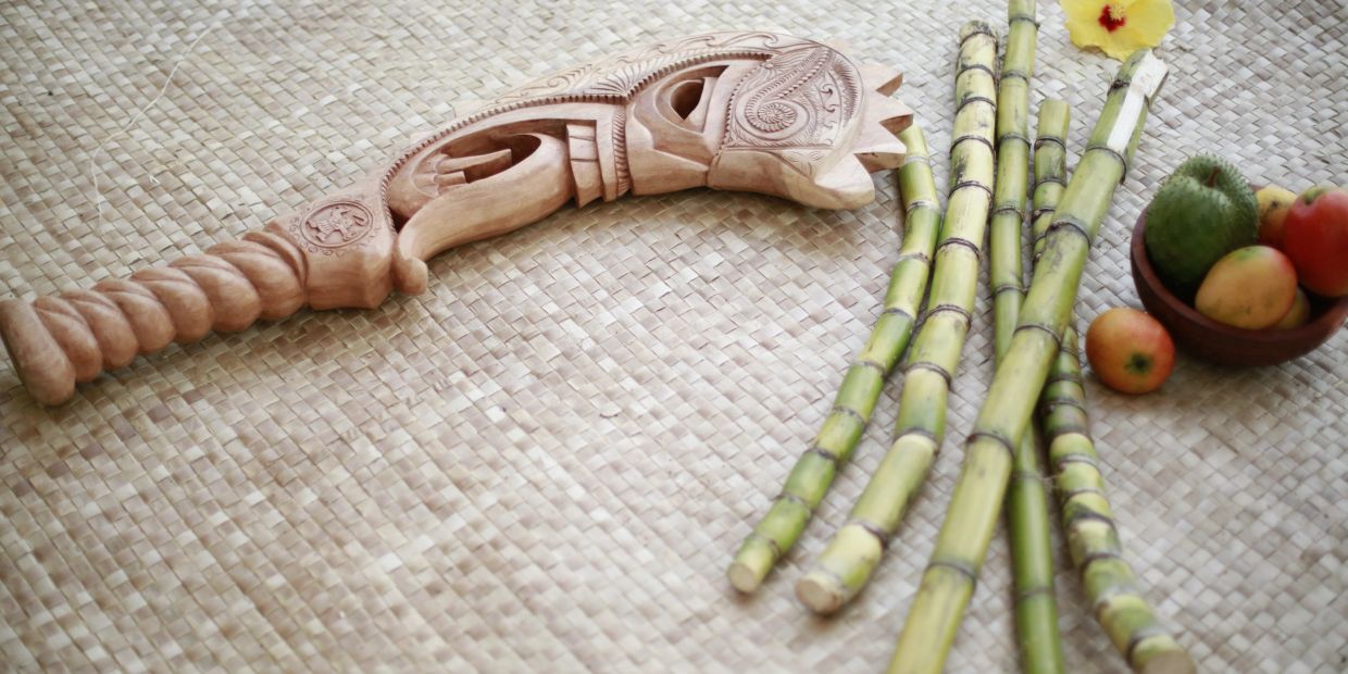 Traditional wooden carving with sugarcane and fruit on woven mat.