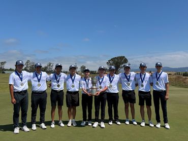 A golf team posing with medals and a trophy on a golf course.