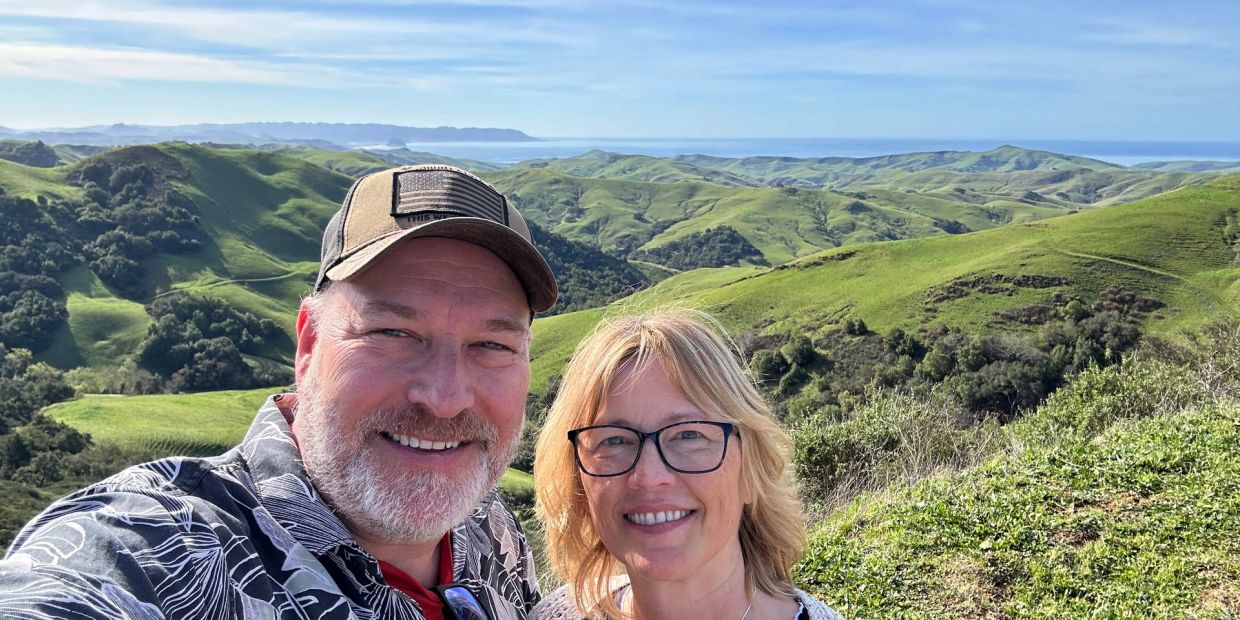 Couple smiling with rolling green hills in the background.