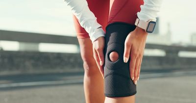 A person wearing a knee brace holds their knee after a sports injury, suggesting pain or discomfort.