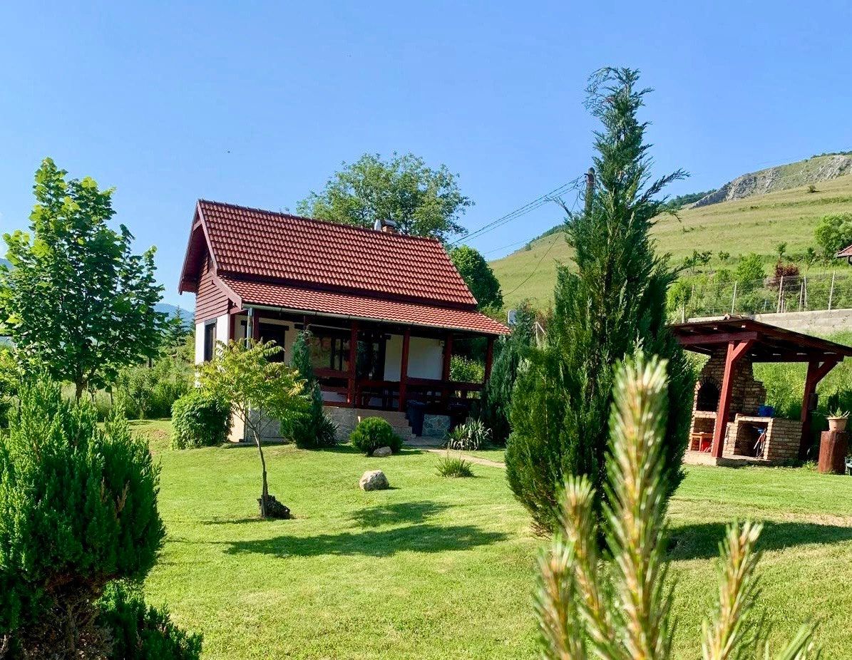Cozy cottage with a red roof surrounded by lush greenery and a clear blue sky.