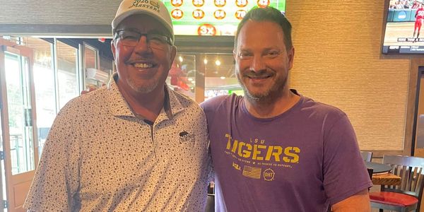 Two smiling men posing together in a casual restaurant setting.