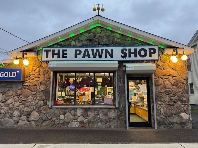 Stone building with a glowing sign that reads 'THE PAWN $HOP' at dusk.