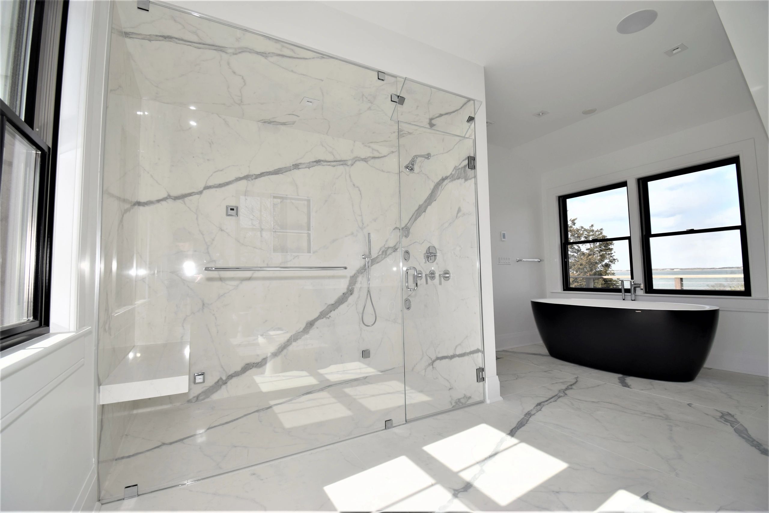 Modern bathroom with marble shower and black bathtub.
