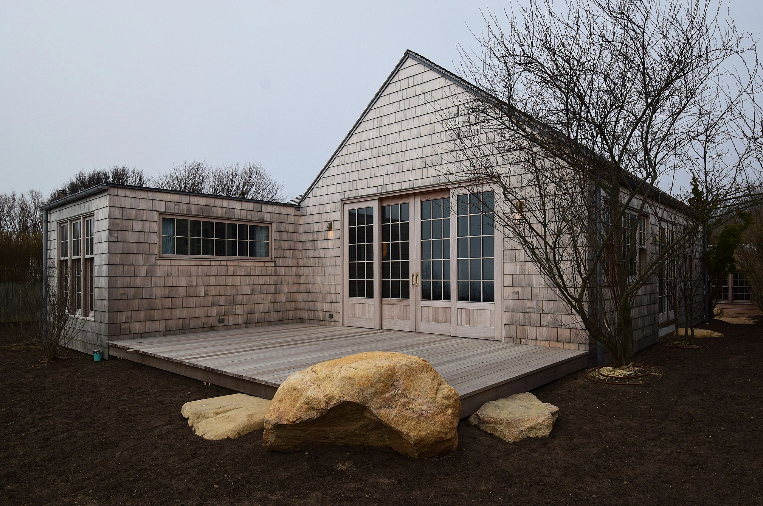 Minimalist wooden house with large rocks and bare trees.