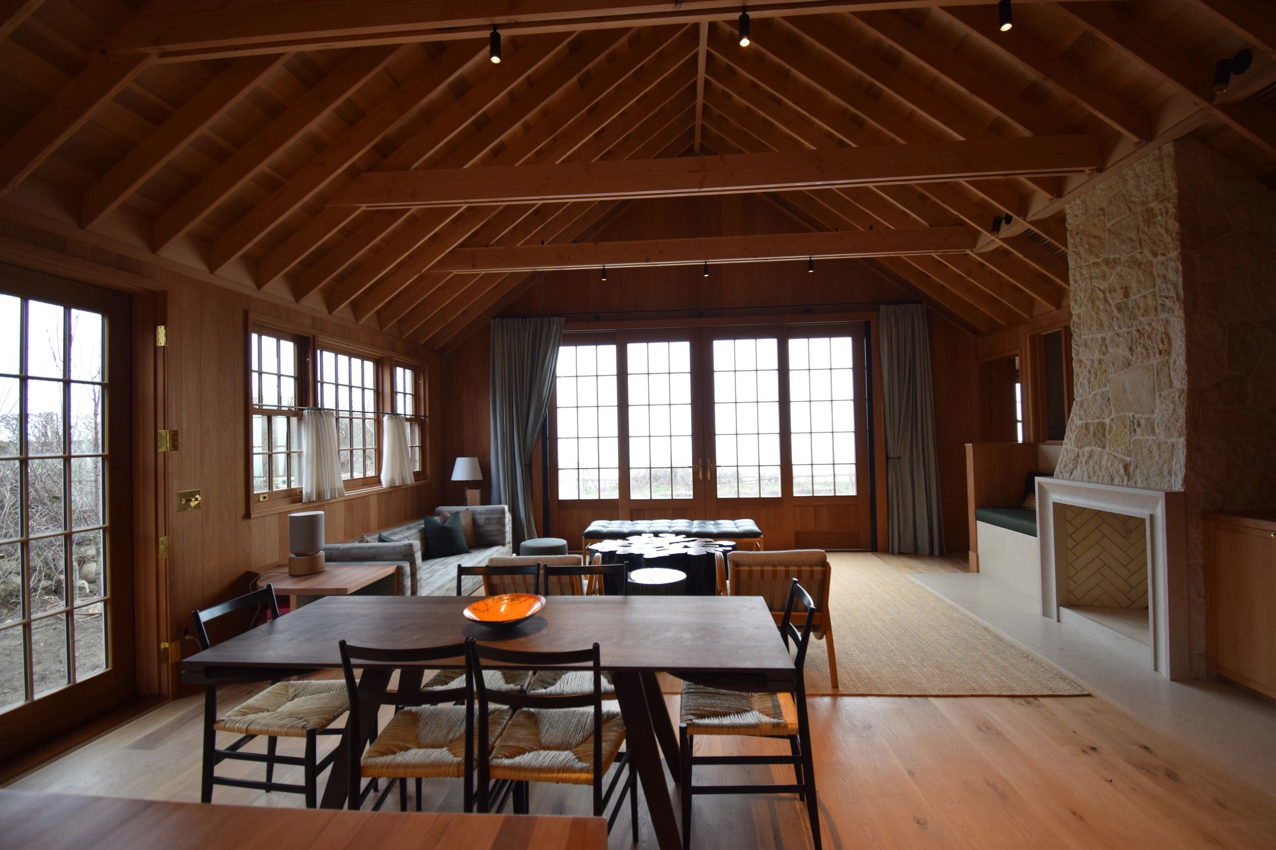 Cozy wooden living room with large windows and stone fireplace.