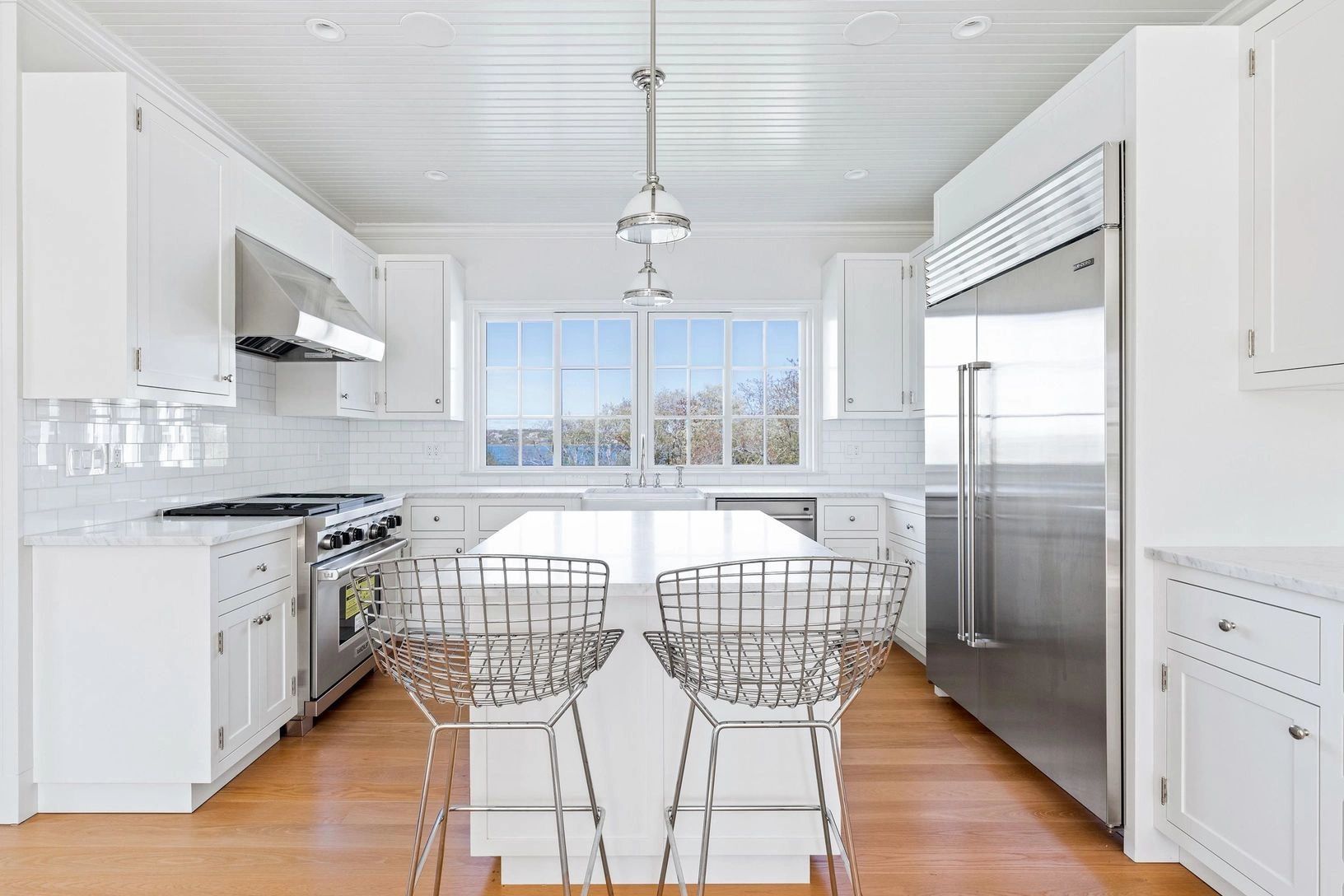 Bright white modern kitchen with metal chairs and wooden floor.