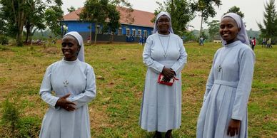Three nuns in gray habits standing outdoors with a building in the background.