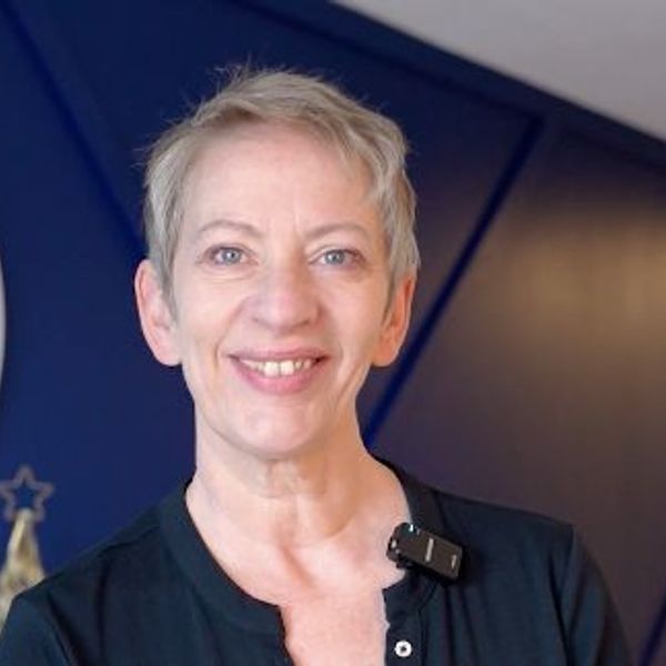 Smiling woman with short blonde hair in a dark top indoors.