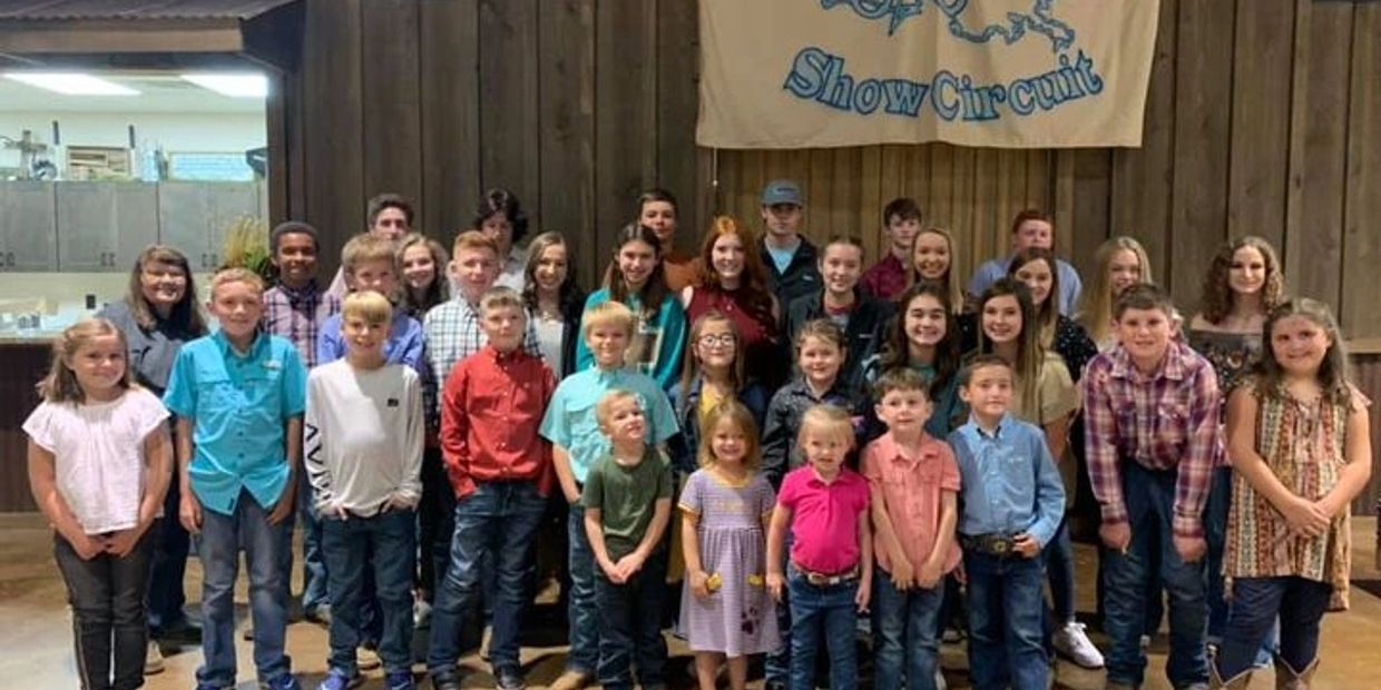 Large group of children and teens posing indoors in front of a wooden wall.