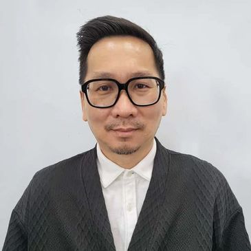 Man wearing black glasses and a black textured jacket over a white shirt.