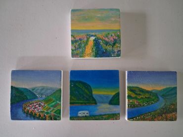 Four small landscape paintings arranged on a white surface.