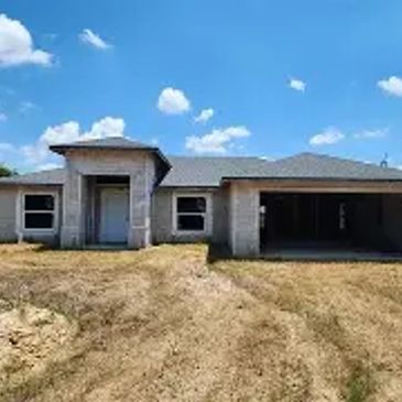 A single-story house under construction with a dry, grassy yard.
