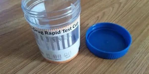 An empty drug rapid test cup with its blue lid on a wooden surface.