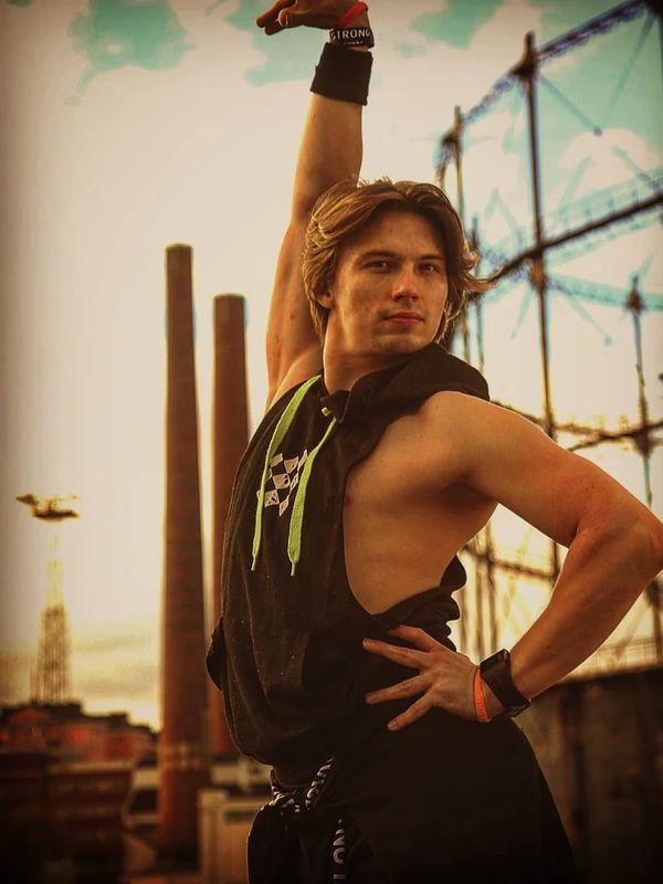 Young man striking a confident pose with one arm raised outdoors at sunset.