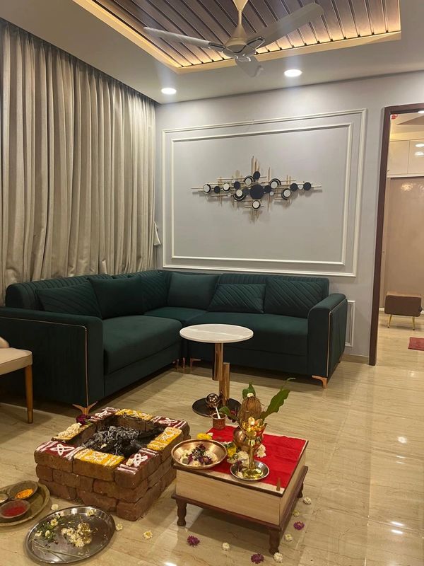 Modern living room with a green sofa and a traditional pooja setup.
