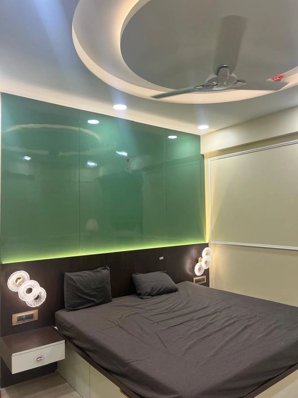 Modern bedroom with green glass accent wall and dark bedding under circular ceiling light.