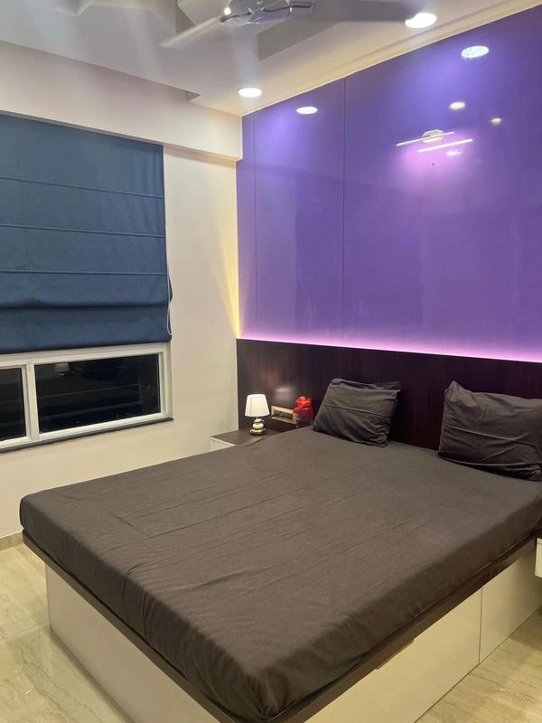 Modern bedroom with purple accent wall and cozy bed.