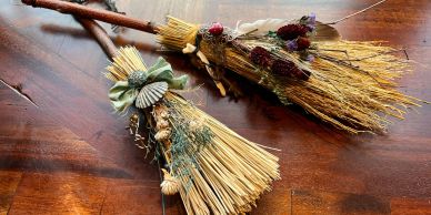 Two decorative straw brooms on a wooden surface.