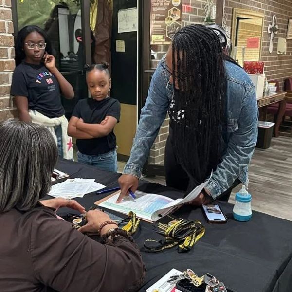 Woman helping another woman at a registration table with kids watching.