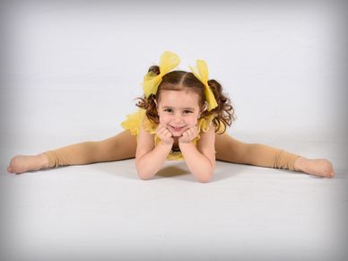 Young girl in yellow costume doing a split with a smile.