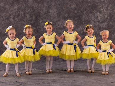 Six young girls in yellow ballet costumes posing for a photo.