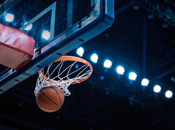A close-up, low-angle shot shows a basketball passing through an orange hoop with a white net