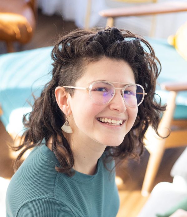 Smiling person with curly hair, glasses, and unique earrings.