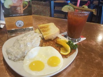 chicken fried steak and gravy on a plate with hash browns and eggs and a bloody mary