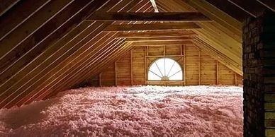 Attic space insulated with pink fiberglass insulation under wooden beams.