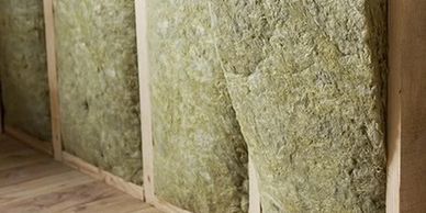 Green insulation panels fitted between wooden studs in a wall frame.