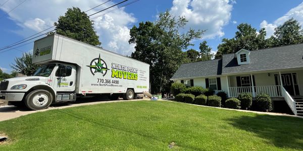 A moving truck parked in front of a suburban house on a sunny day North Point Movers.
