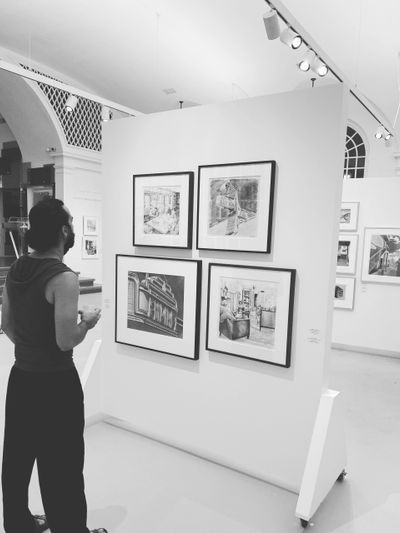 A man views framed artwork in a modern gallery.