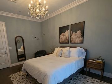 Cozy bedroom with white bedding, cloud artwork, and a patterned rug.