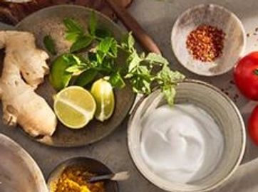 Fresh ingredients including ginger, lime, mint, spices, and yogurt in bowls.